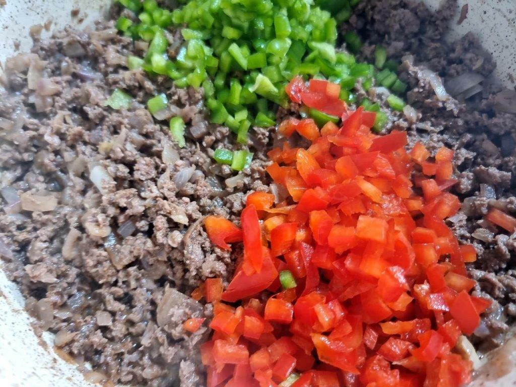 Adding green and red bell peppers to ground beef chili.